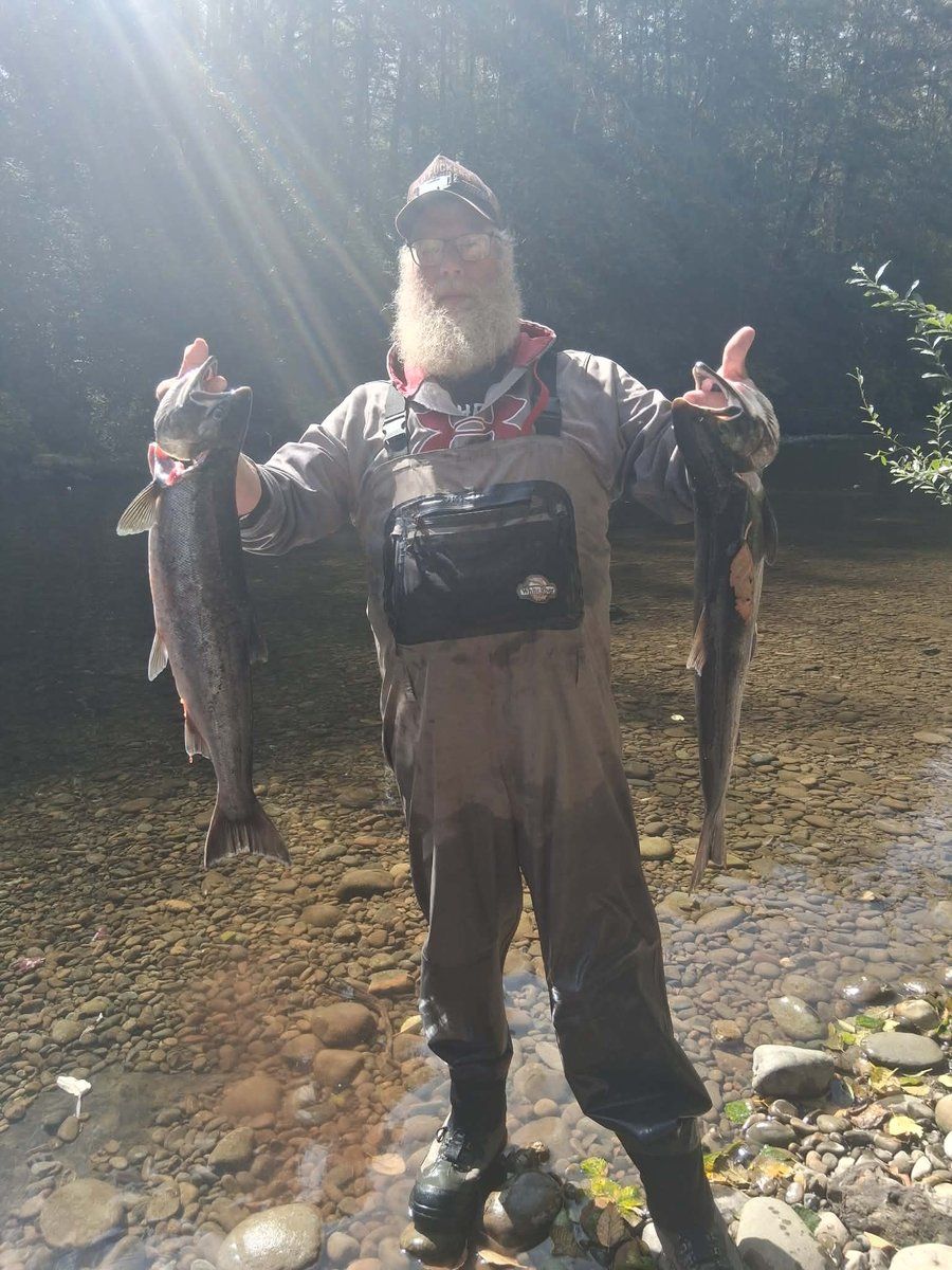 Your guide standing in the river holding a salmon in each hand, forest along the bank behind him