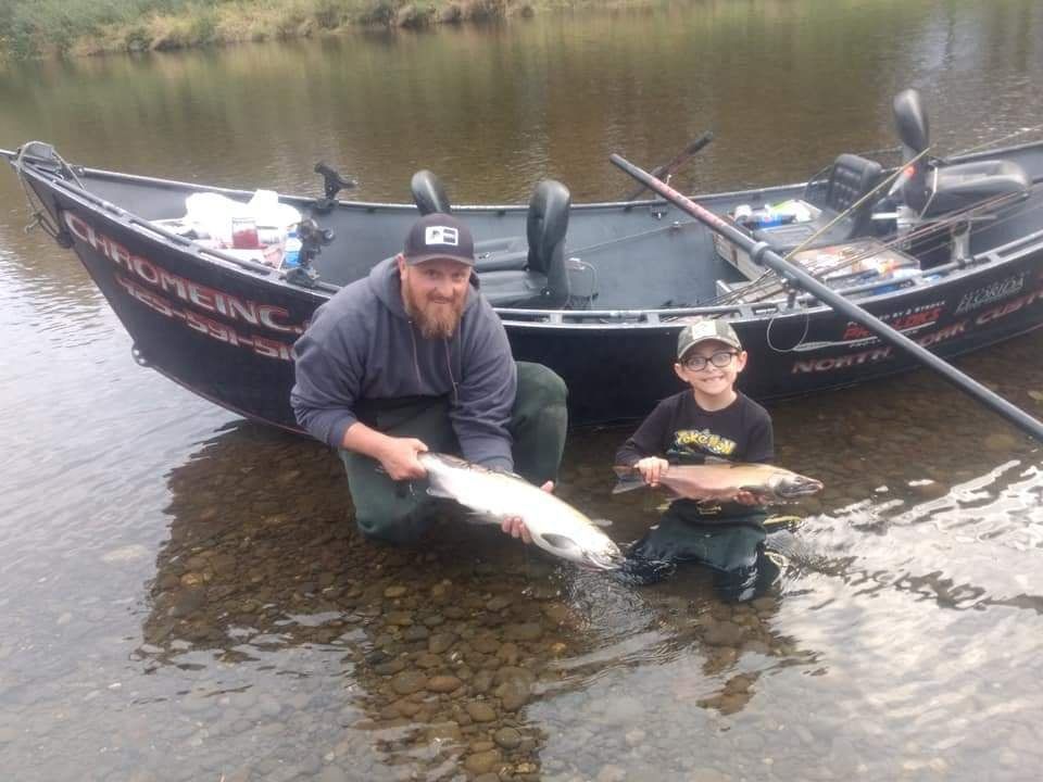A guide and a young angler kneeling in the river holding salmon beside a second drift boat