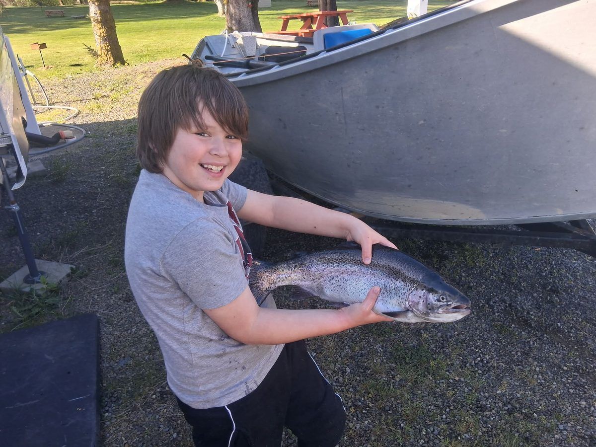 A young angler holding a large salmon beside the drift boat at the launch