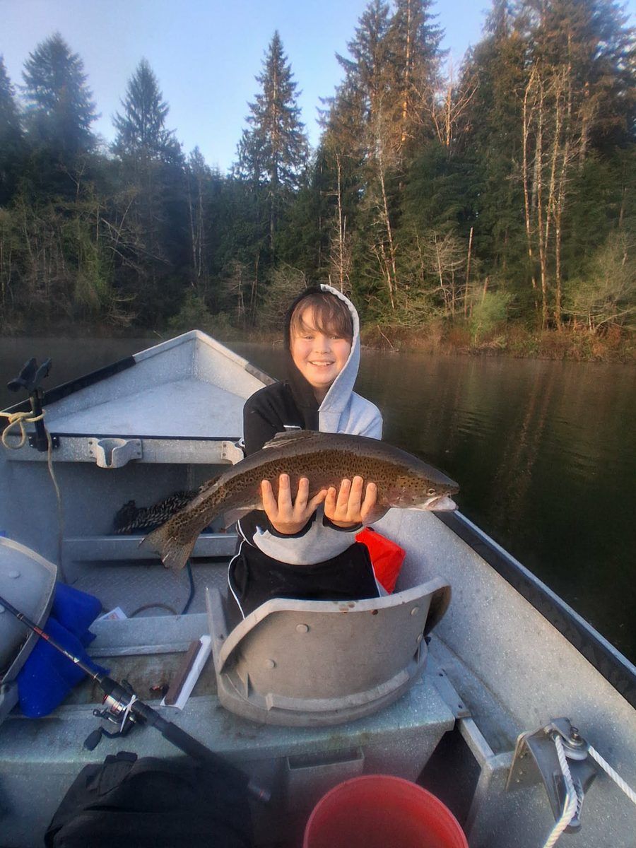 A young angler in a hooded sweatshirt holding a trout in the drift boat at first light